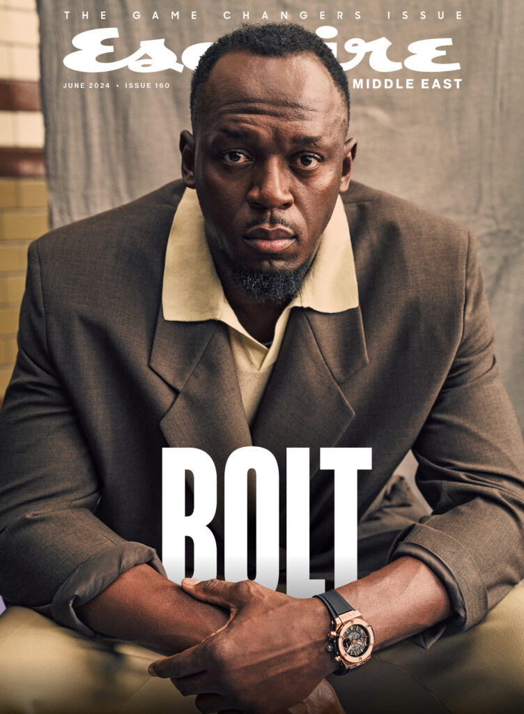 Esquire Middle East magazine cover featuring Idris Elba in a tailored brown suit seated in a studio portrait.