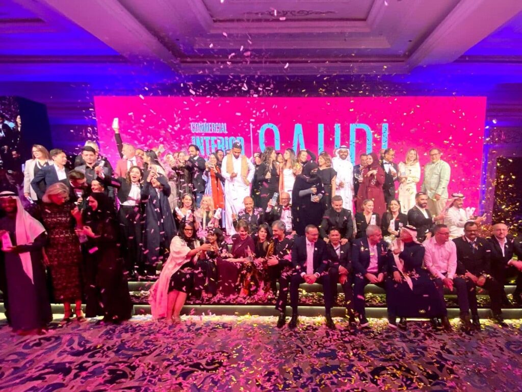 A large group of professionals standing on a stage under colorful lighting during an awards ceremony, celebrating achievements in design.