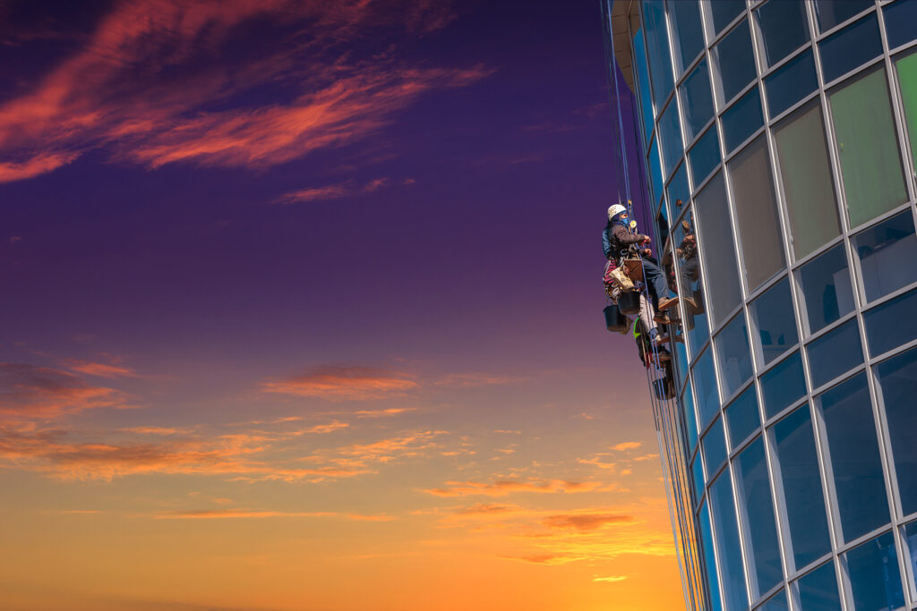 Rope access technician performing exterior maintenance on a high-rise glass building representing Facilities Management Middle East industry services.