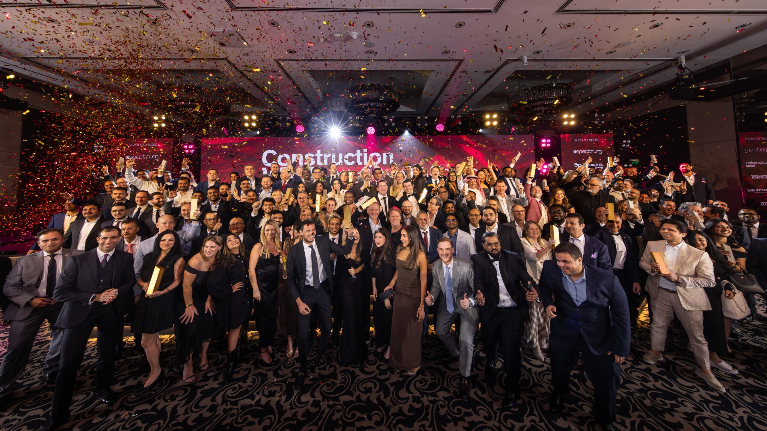 Large group of construction industry professionals celebrating on stage at the Construction Week Middle East awards event with confetti and trophies.