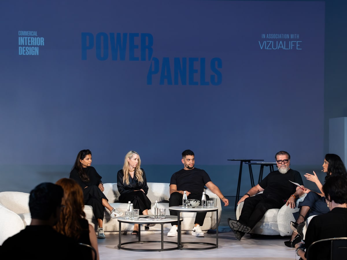 A panel discussion with five design professionals seated on a stage under a blue backdrop reading “Power Panels,” speaking to an audience during a Commercial Interior Design event.